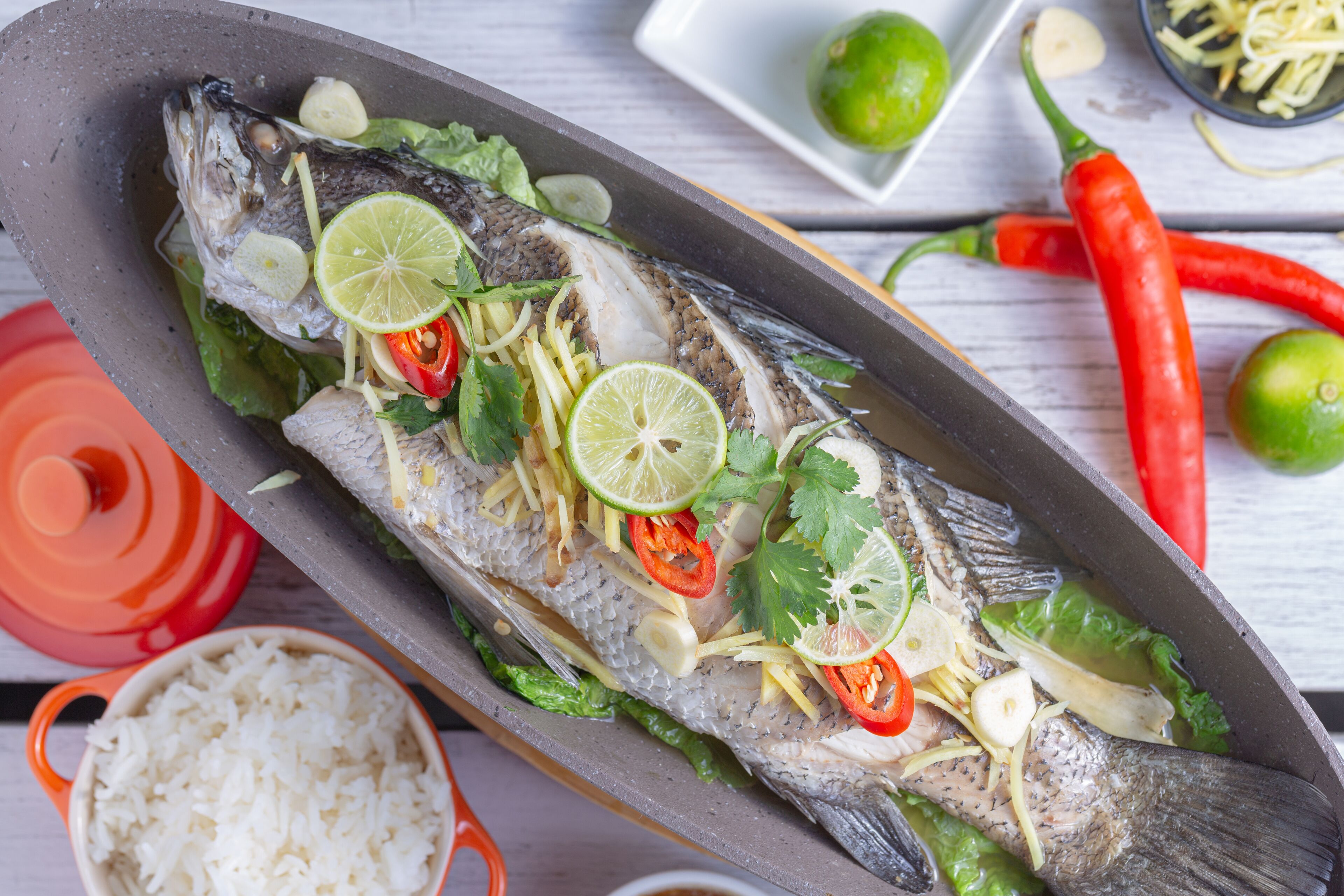 Un pescado entero aderezado con limón, chile y hierbas, rodeado de ingredientes como ajo y lechuga.