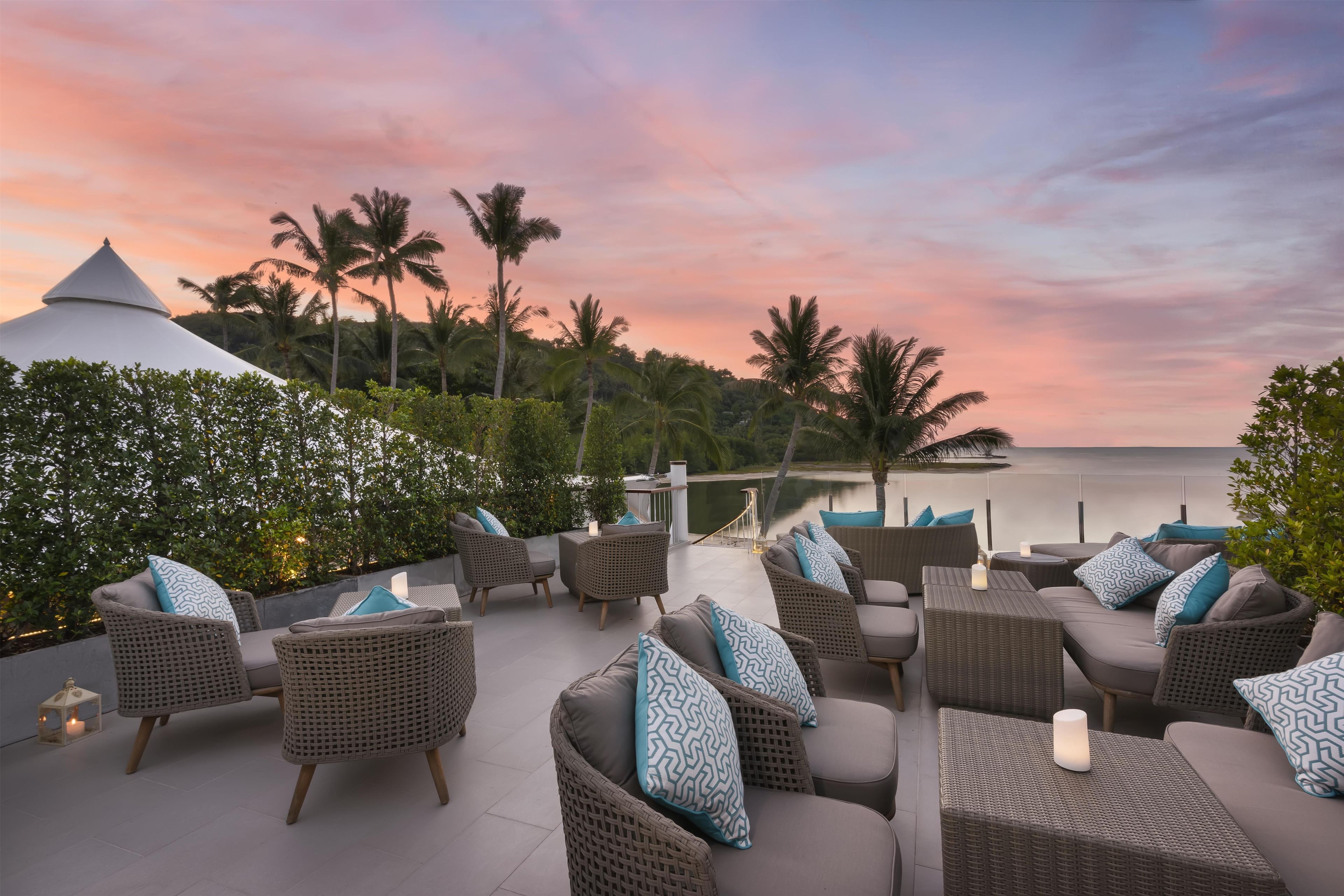 Una terraza con mobiliario de mimbre y vista al mar al atardecer.