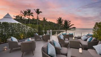 Una terraza con mobiliario de mimbre y vista al mar al atardecer.