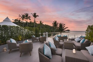 Una terraza con mobiliario de mimbre y vista al mar al atardecer.