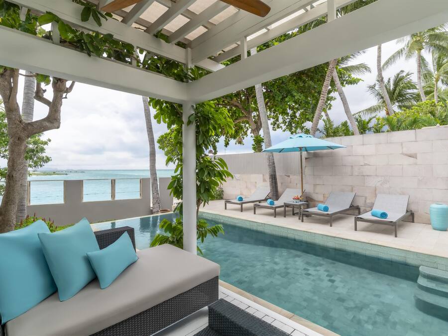 Área da piscina com espreguiçadeiras, um espaço de estar com almofadas e vista para o oceano.
