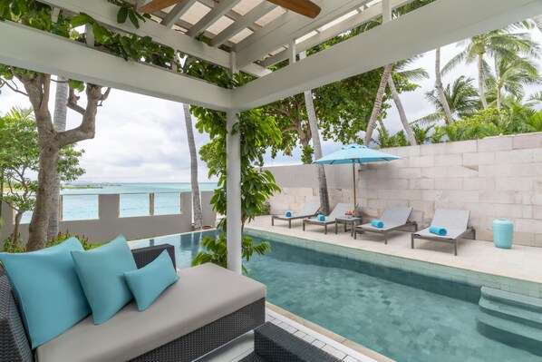 A poolside area with lounge chairs, a seating area with cushions, and a view of the ocean.