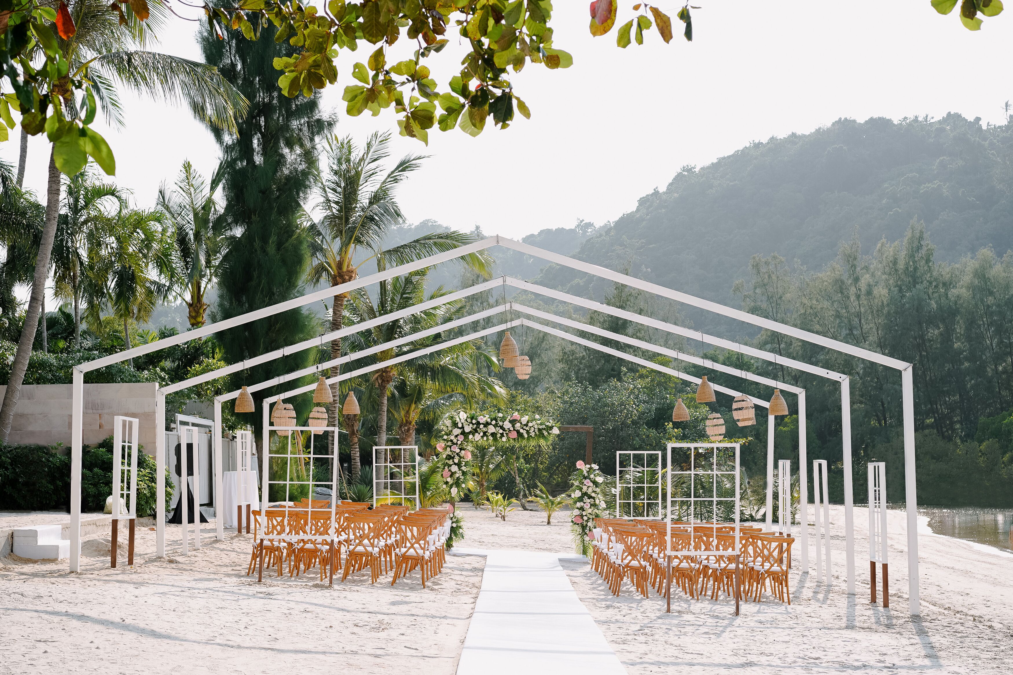 Montaje de boda en la playa con un arco blanco y sillas de madera.