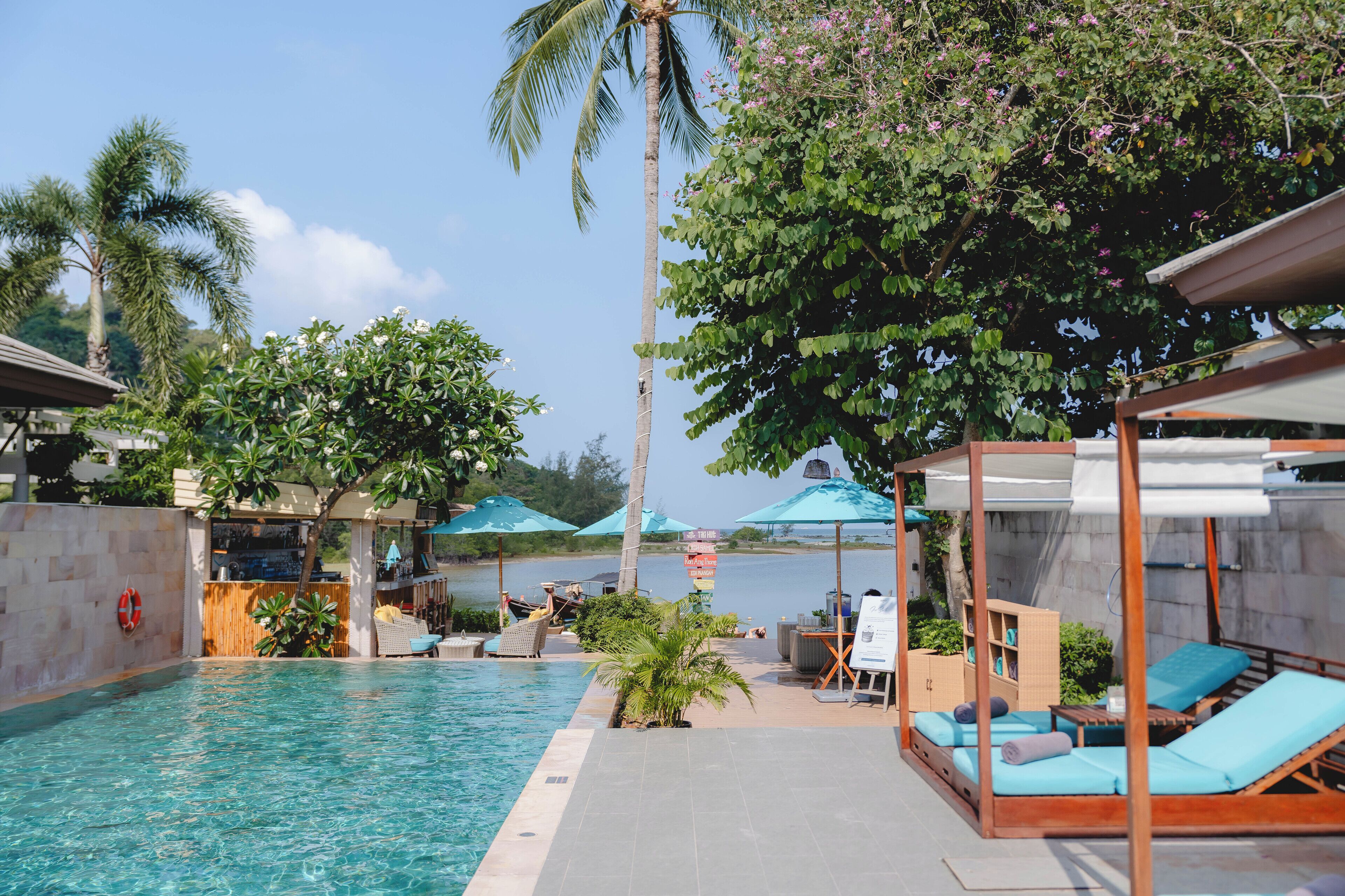 A poolside area with lounge chairs, umbrellas, and a view of the sea.