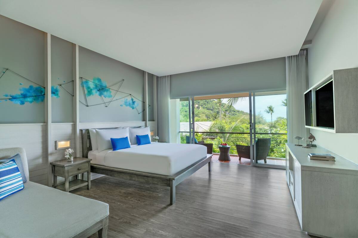A modern hotel room with a large bed, bedside tables, a desk, and a TV.