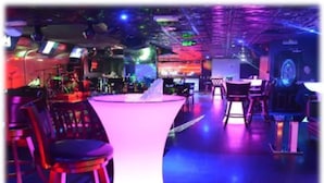 A bar area with stools and a bar counter, illuminated by colorful lighting. - Royal Falcon Hotel (Dubai)