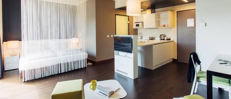Una habitación de hotel moderna con una cama, una mesita con un libro y una taza, una kitchenette y un comedor.