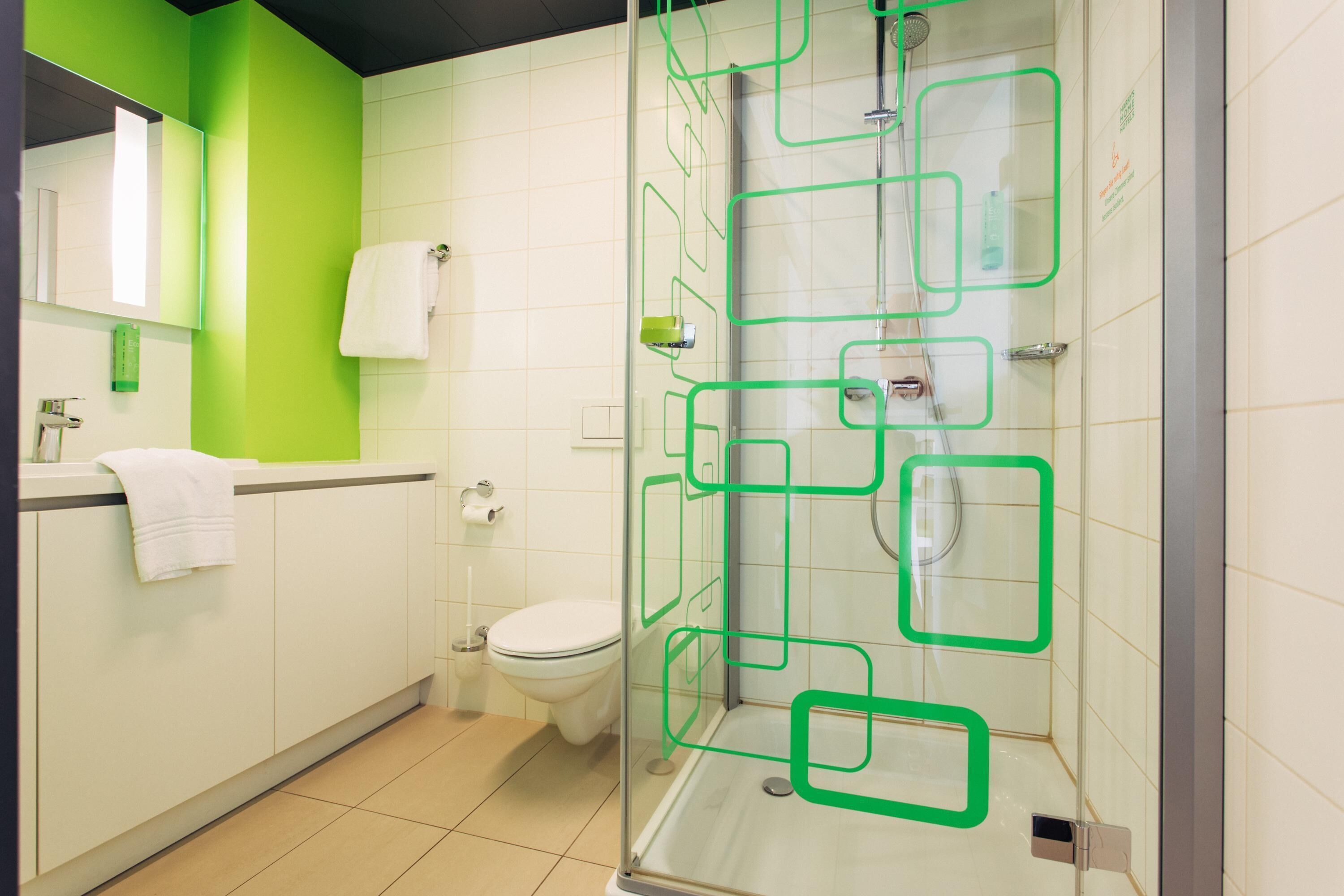 Une salle de bain moderne avec une douche à parois de verre, des toilettes et un lavabo devant un mur vert.