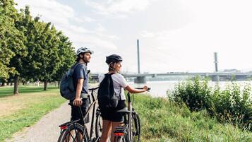 Two people on bicycles on a path with a river and a bridge in the background.