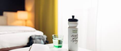 A hotel room with a bed, a bedside table with a book and a water bottle, and a glass of water.