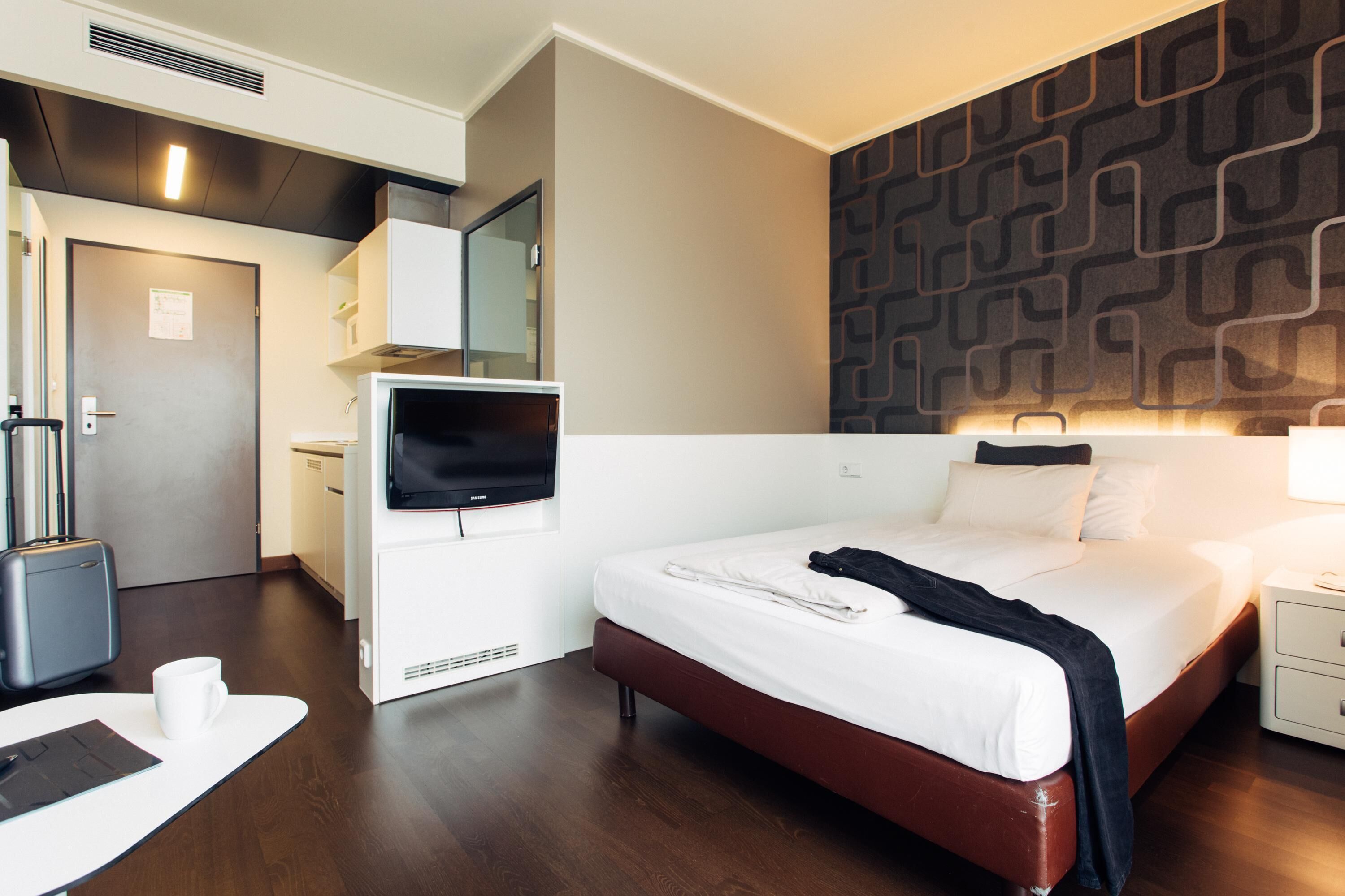 A hotel room with a bed, a desk, a television, a mirror, and a patterned wall.