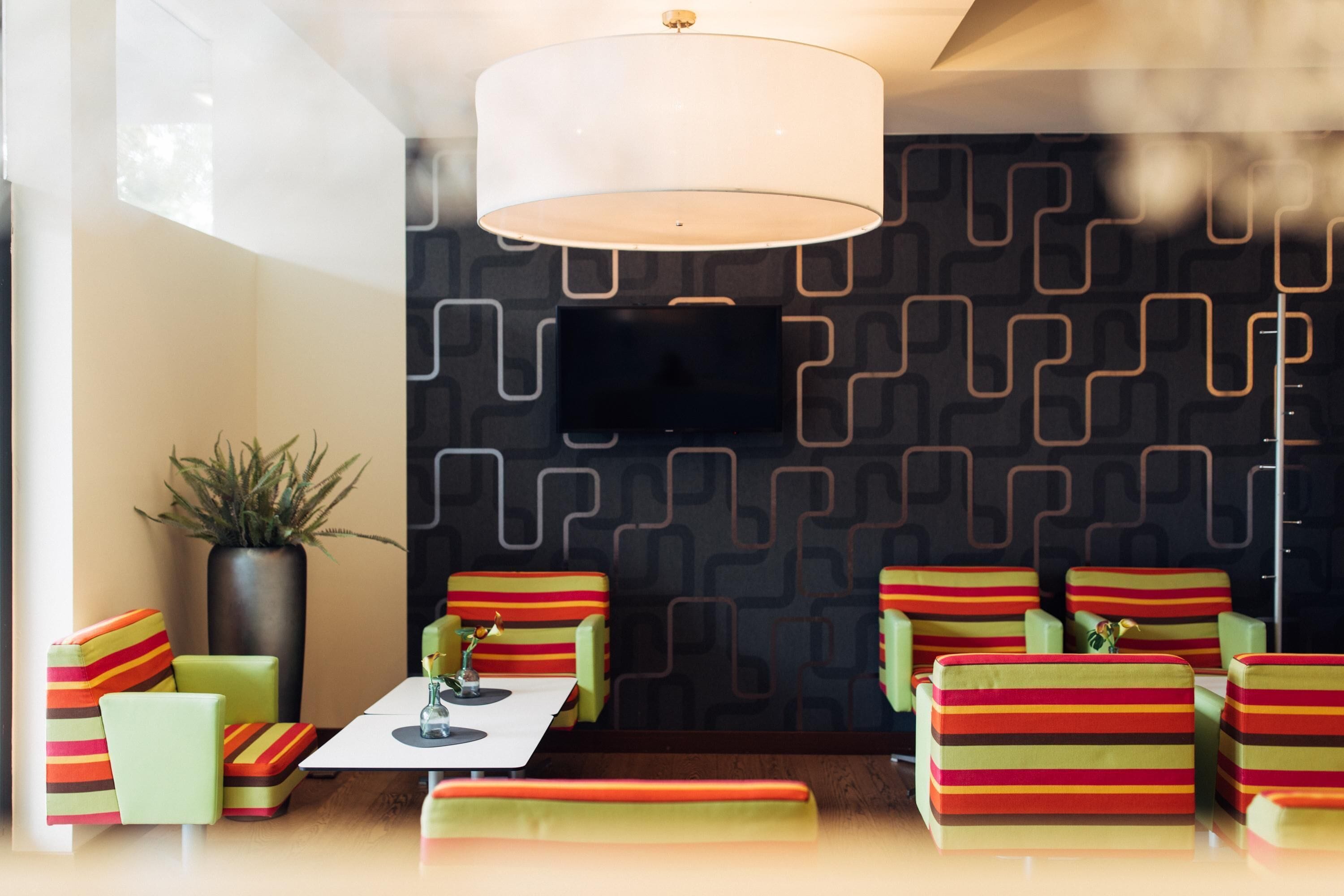 A modern lounge area with a patterned wall, a flat-screen TV, and colorful striped seating.