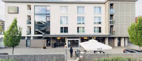 A modern hotel with a flat facade, multiple windows, and a Coca-Cola branded outdoor seating area.