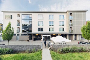 Un hotel moderno con fachada plana, múltiples ventanales y un área de estar exterior con la marca Coca-Cola.