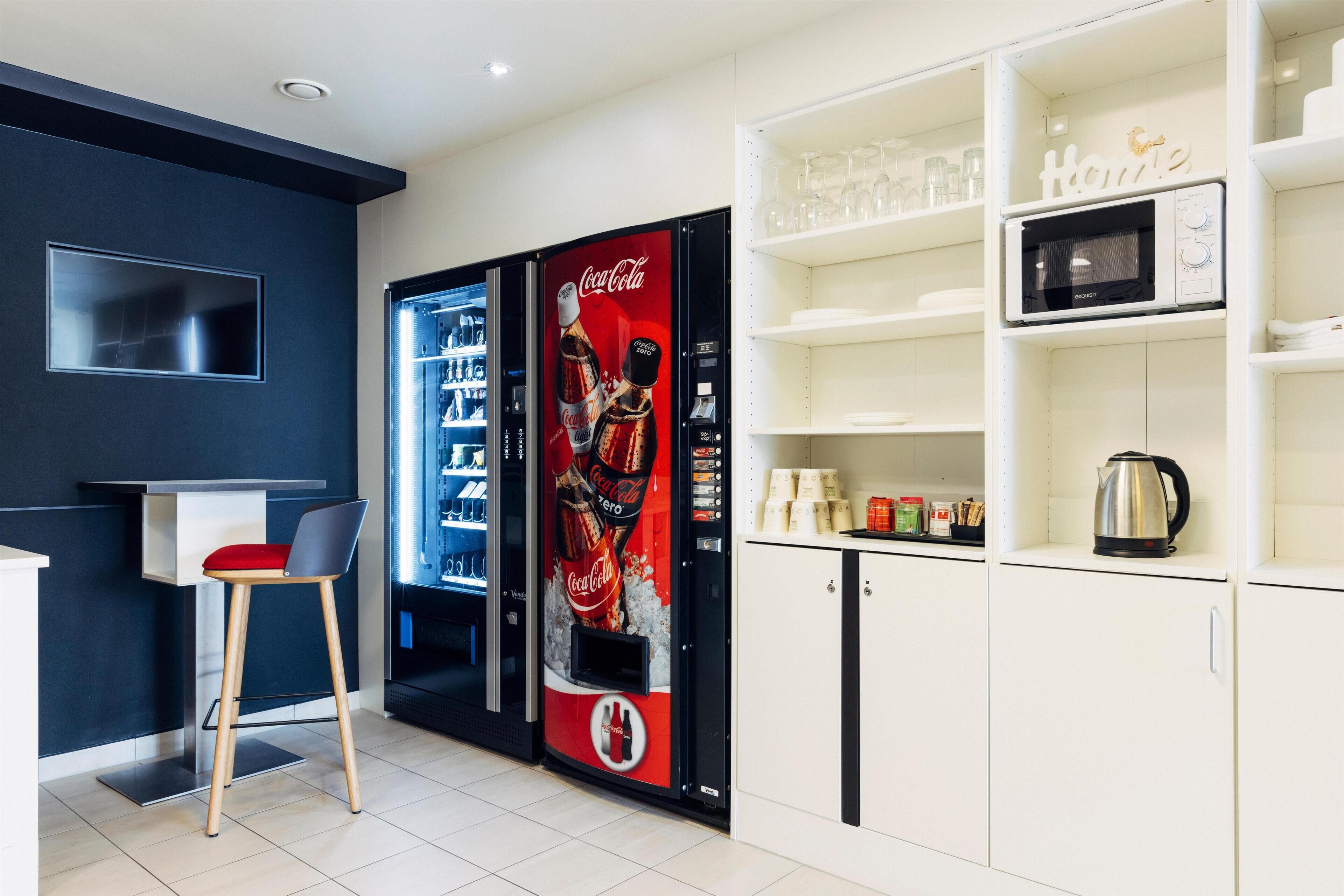Une cuisine moderne équipée d’un distributeur automatique de Coca-Cola, d’un four à micro-ondes et d’une bouilloire posés sur le plan de travail.