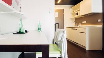 Cocina moderna con armarios blancos, un lavamanos de acero inoxidable y un microondas. Hay una mesa de comedor con dos botellas verdes y vasos.