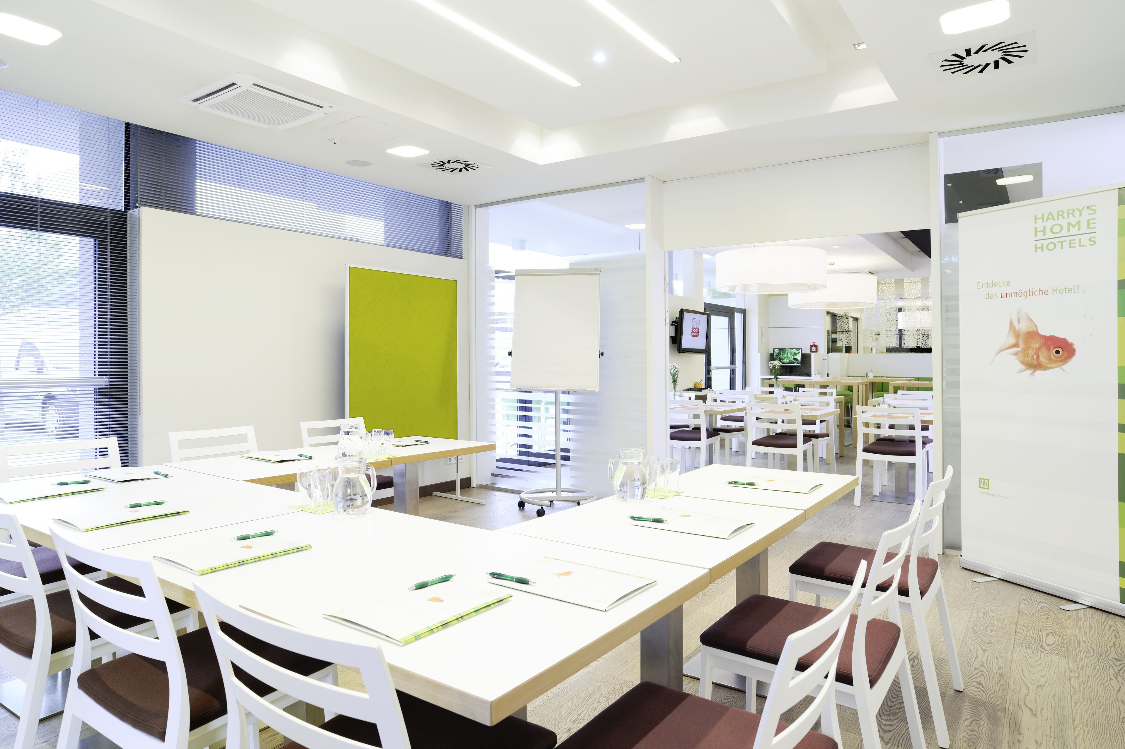 Una sala de conferències d'hotel moderna amb taules blanques, cadires marrons amb reposabocs i una pissarra blanca gran.