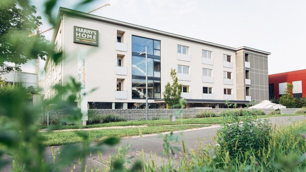 A modern hotel building with a sign reading "Harry's Home." It features a large glass facade, multiple balconies, and a stone base. - harry’s home Linz-Urfahr hotel & apartments (Linz)