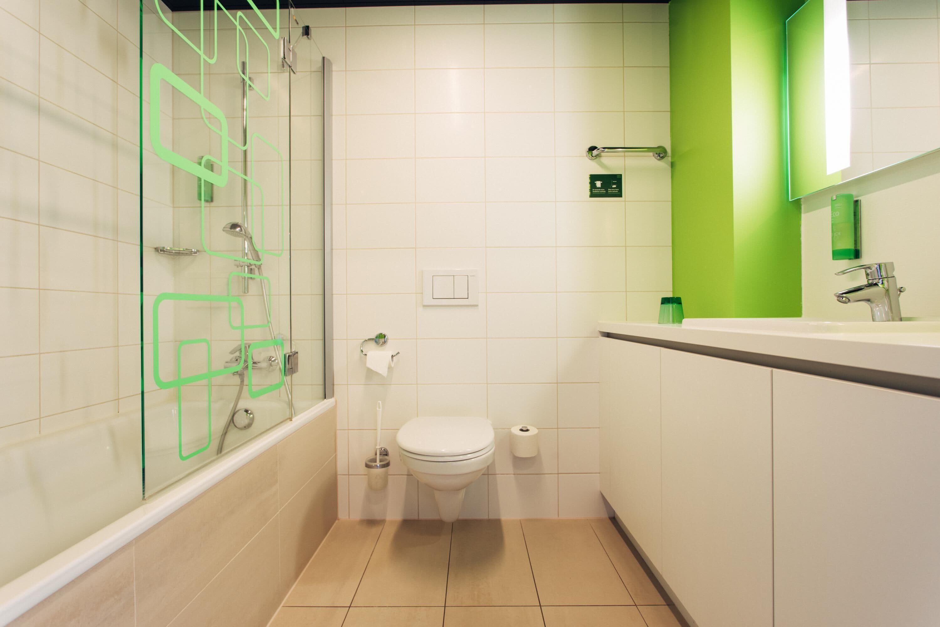 A modern bathroom with a glass-enclosed shower, a toilet, and a sink with a green accent wall.