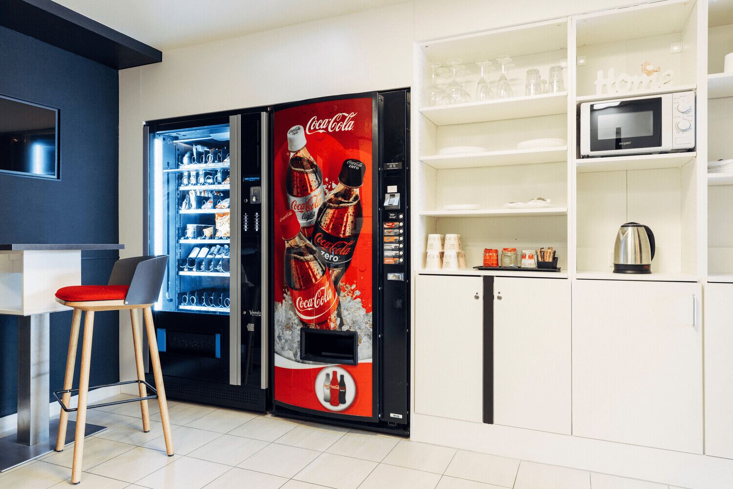 A modern kitchen with a Coca-Cola refrigerator, a microwave, and a kettle on the counter.