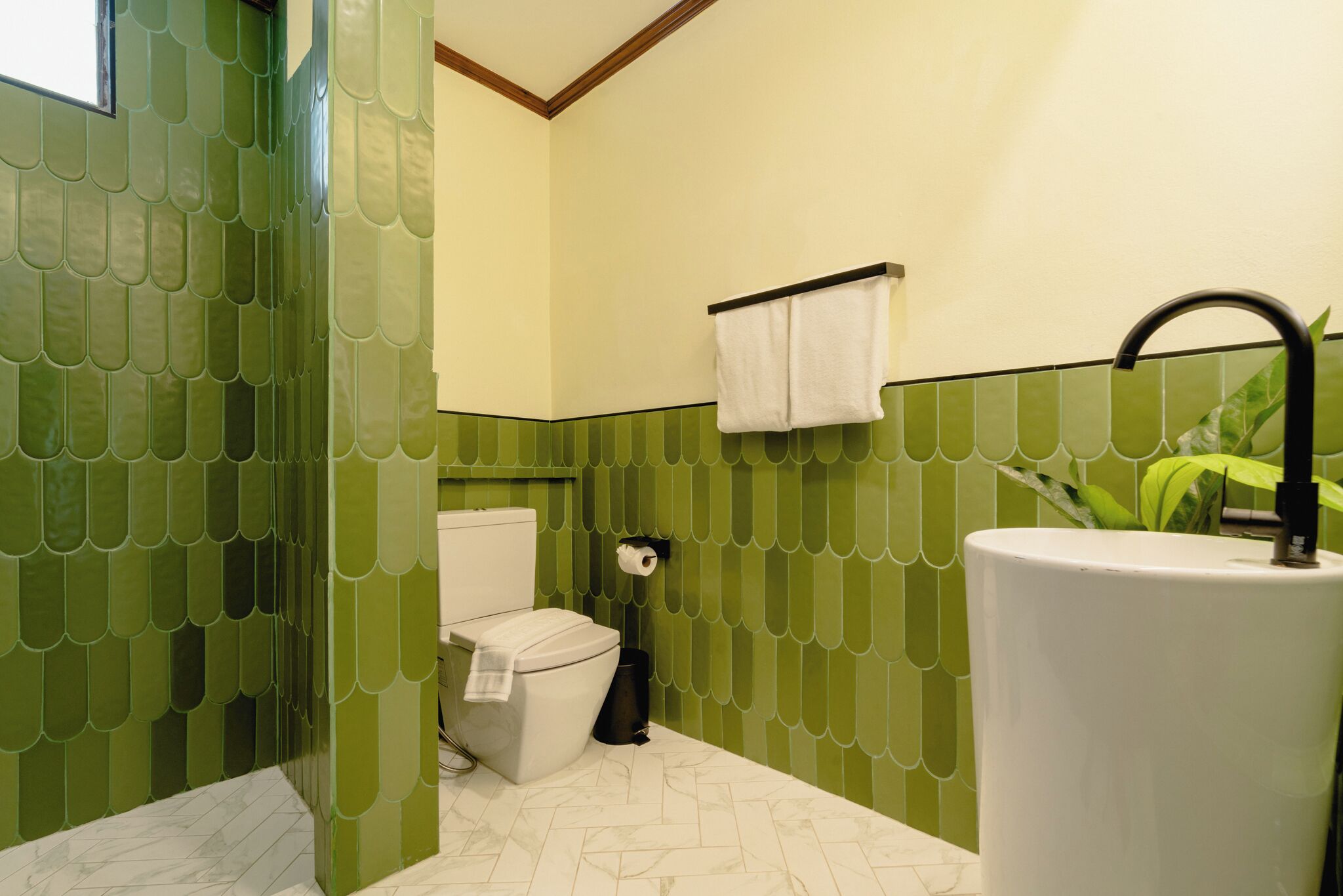A bathroom with green tiled walls, a white toilet, a sink with a black faucet, and a towel rack with a white towel.