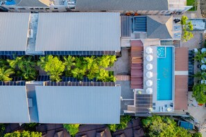 An aerial view of a hotel with a rooftop pool, solar panels, and palm trees.