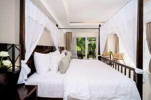 A large bed with white bedding, a nightstand with a vase of flowers, and a view of a balcony with outdoor furniture.