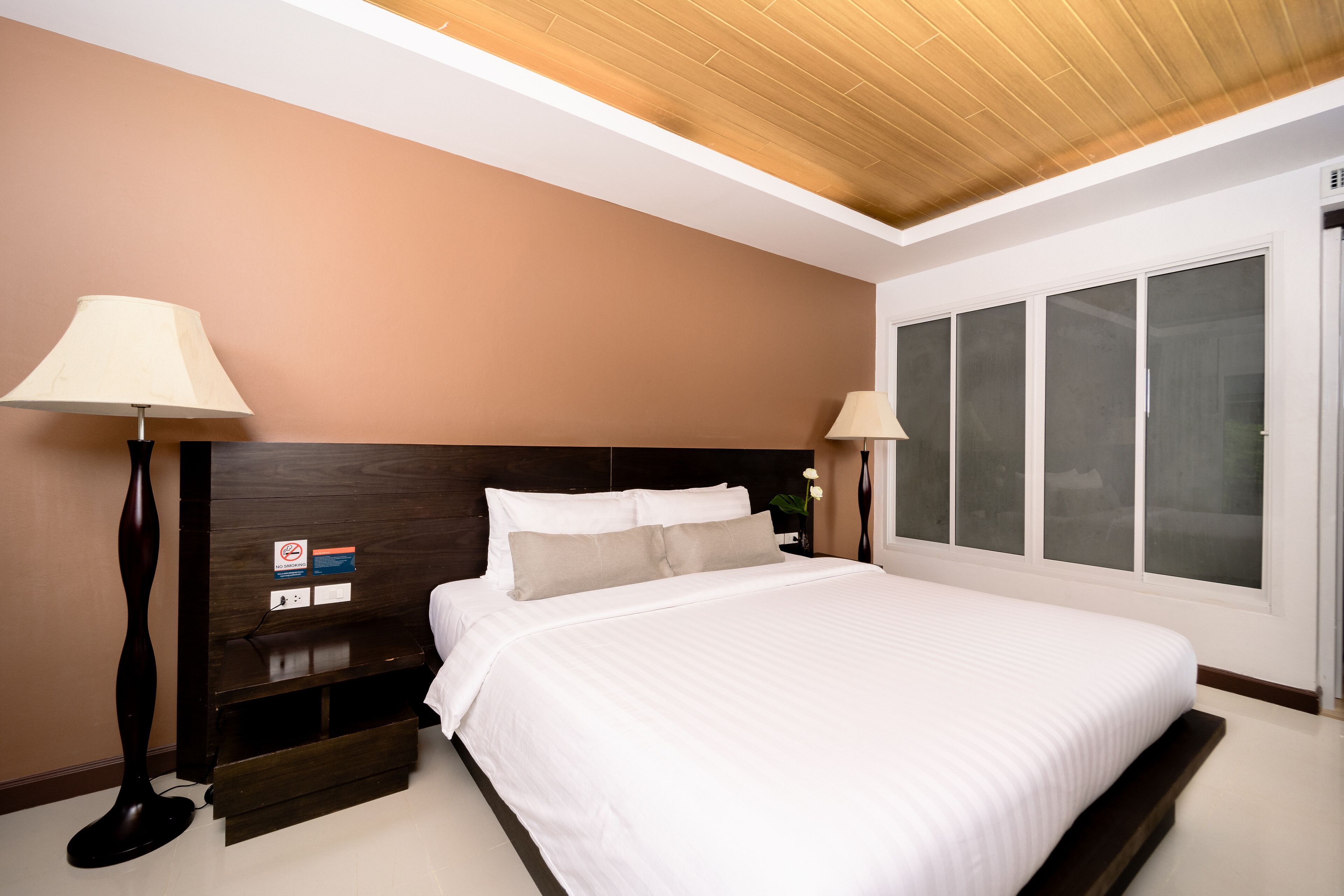 A modern bedroom with a large bed, wooden headboard, bedside lamps, and a window with frosted glass.
