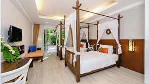 A four-poster bed with white linens, a television on the wall, and a desk with a plant.