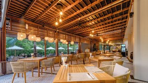 A spacious outdoor dining area with wooden tables and chairs, large windows, and hanging light fixtures. - Railay Princess Resort & Spa (Krabi)