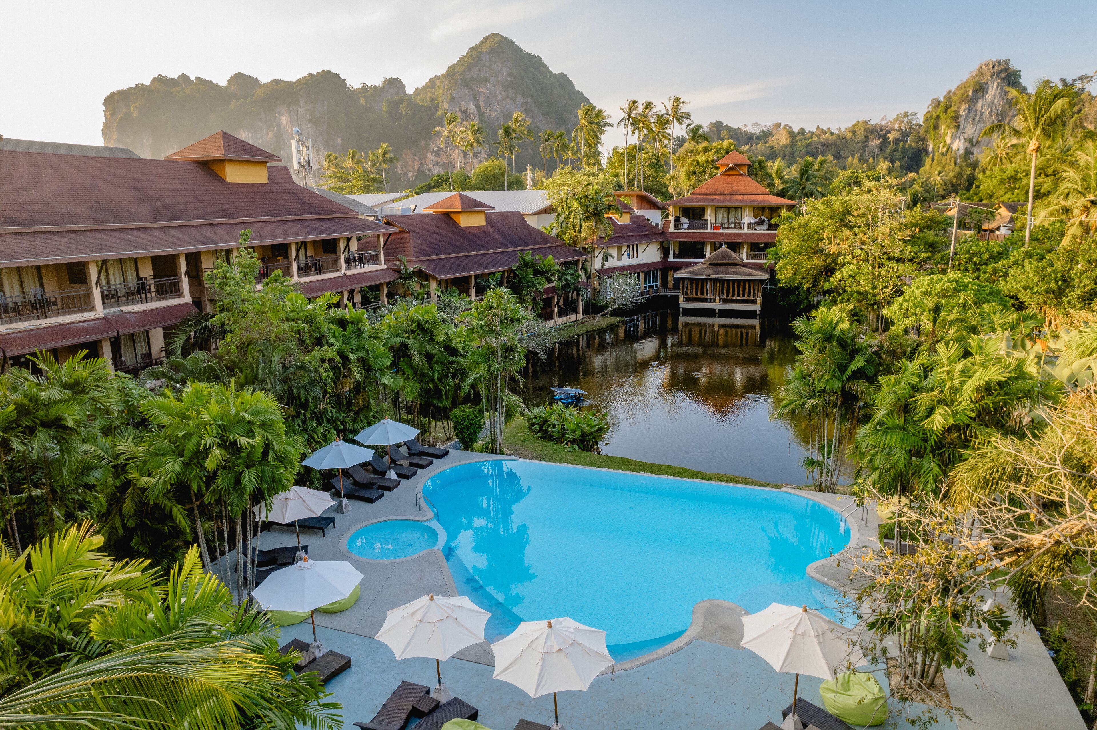 A resort with a large swimming pool surrounded by lush greenery and palm trees.