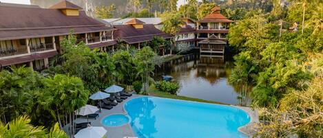 A resort with a large swimming pool surrounded by lush greenery and palm trees.