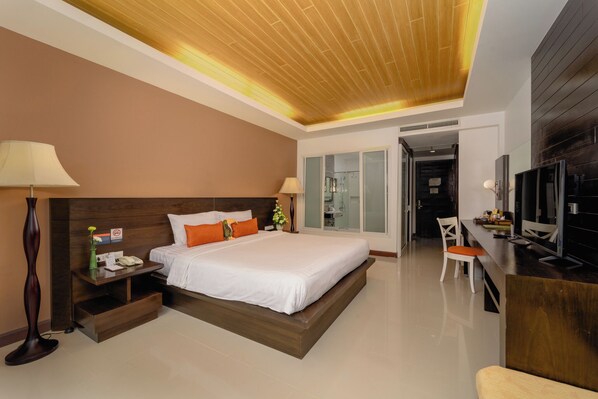 Una habitación de hotel moderna con una cama grande, mesitas de noche, un escritorio con una silla, un televisor y un baño visible a través de una puerta de vidrio.