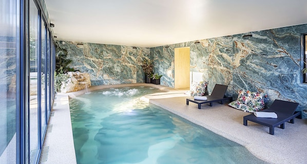 A spa area with a hot tub, lounge chairs, and a stone wall. - Best Western Amarys Hotel & Spa (Rambouillet)