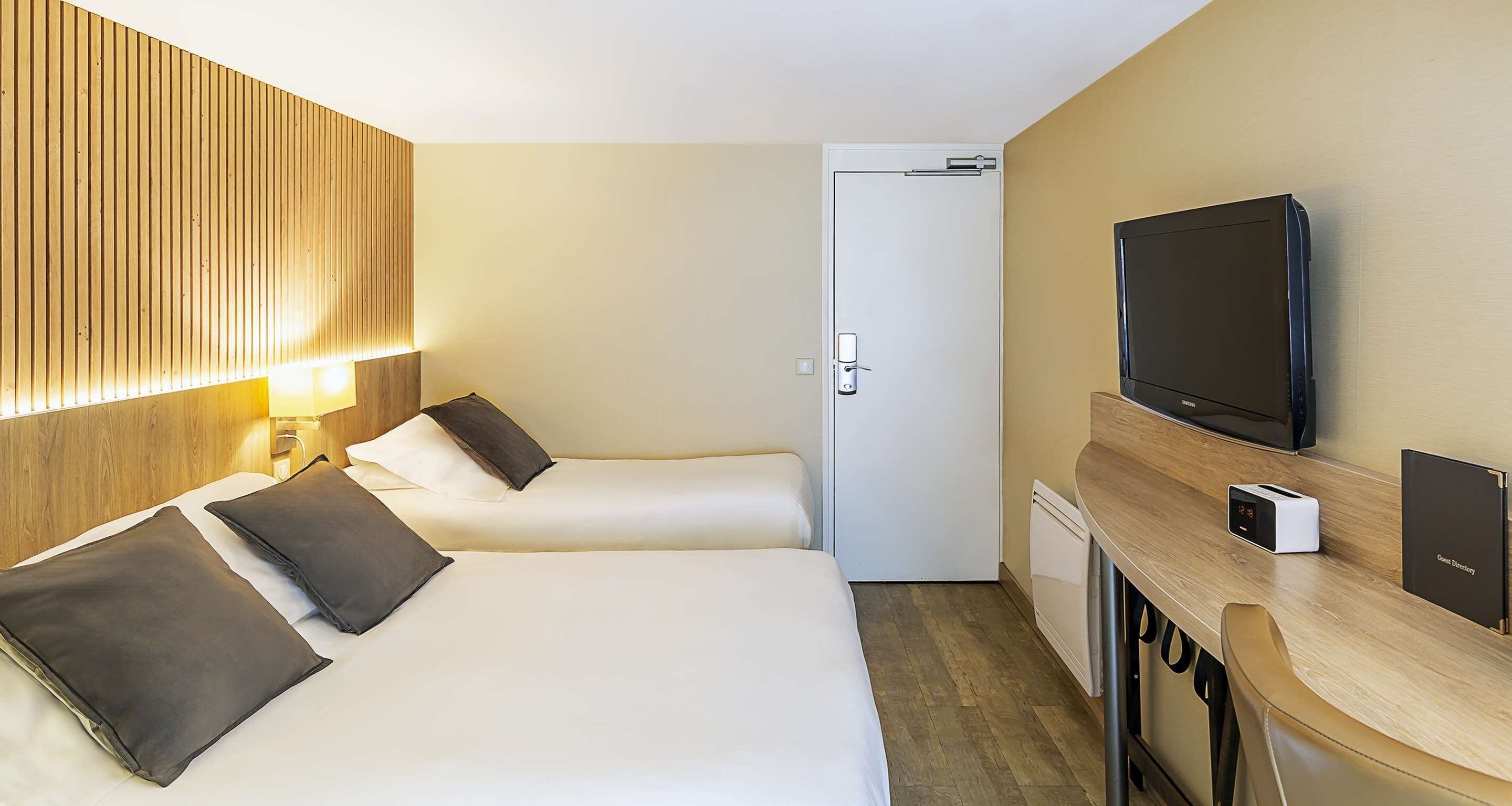Habitación de hotel con dos camas, un televisor, un escritorio y un tostador, y una puerta.
