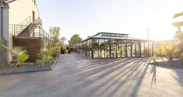 A modern building with a glass conservatory, a staircase, and a paved walkway with plants.
