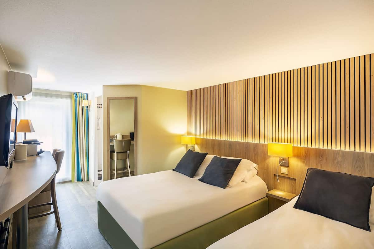 A hotel room with two beds, a desk, and a chair.