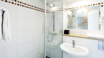 Un baño moderno con cabina de ducha de vidrio, un lavamanos blanco y un espejo con toallero.
