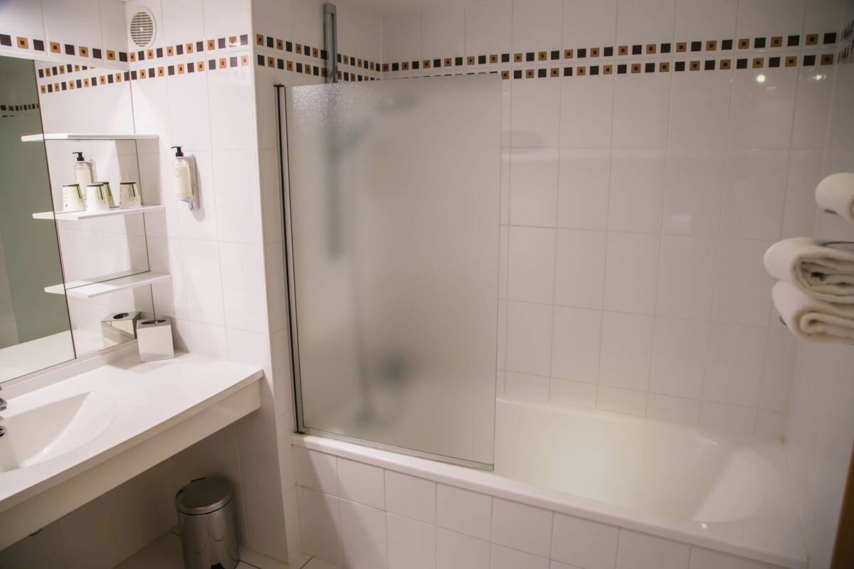 A modern bathroom with a glass shower enclosure, a white sink, and a mirror with toiletries.
