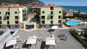 Un hotel con varias plantas, piscina exterior y zona de playa con sombrillas y tumbonas.