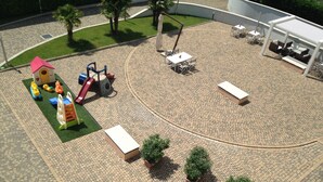 Un parque infantil con estructuras de juego y una zona de estar circular con mesas y bancos.