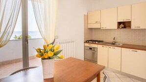 A modern kitchen with light-colored cabinets, a stove, and a sink. There is a window with sheer curtains and a vase of yellow flowers on the counter. - Residence Sant'Anna (Pietra Ligure)