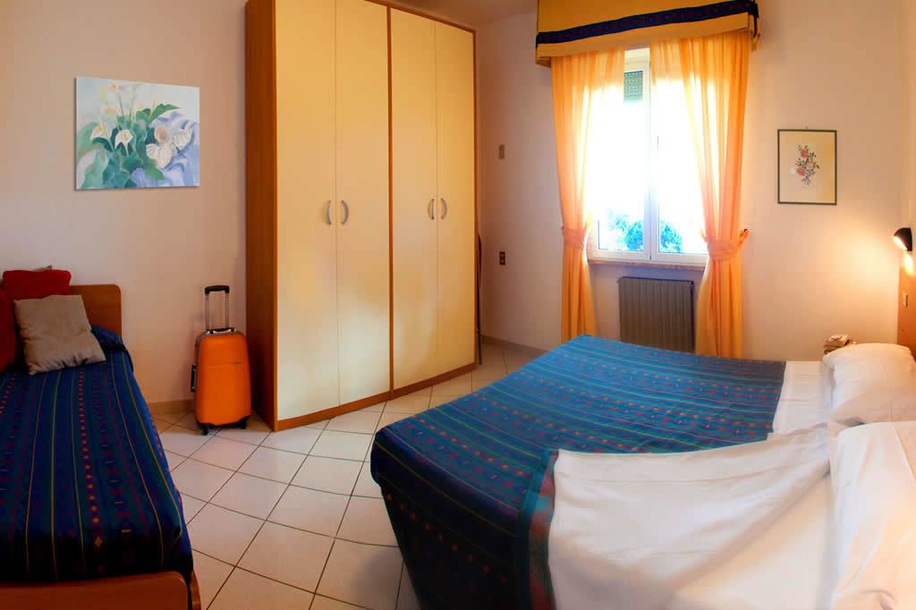Een hotelkamer met twee bedden, een garderobe, een koffer en een raam met gordijnen.