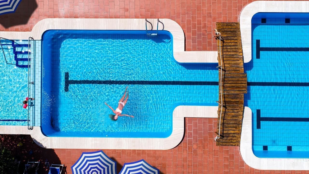 A rectangular swimming pool with a diving board, surrounded by a brick wall and a wooden deck.