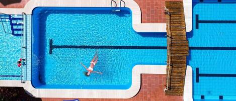 A rectangular swimming pool with a diving board, surrounded by a brick wall and a wooden deck.