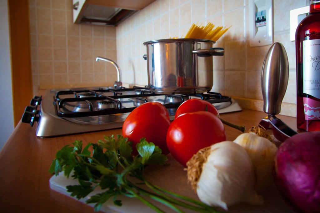 Una encimera de cocina con estufa a gas, ollas, tomates, ajo y una botella de aceite de oliva.