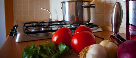 Una encimera de cocina con estufa a gas, ollas, tomates, ajo y una botella de aceite de oliva.
