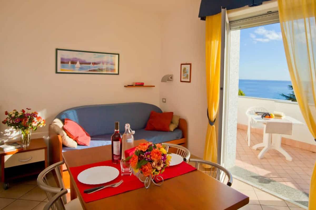 A cozy room with a sofa, dining table, and a view of the sea.