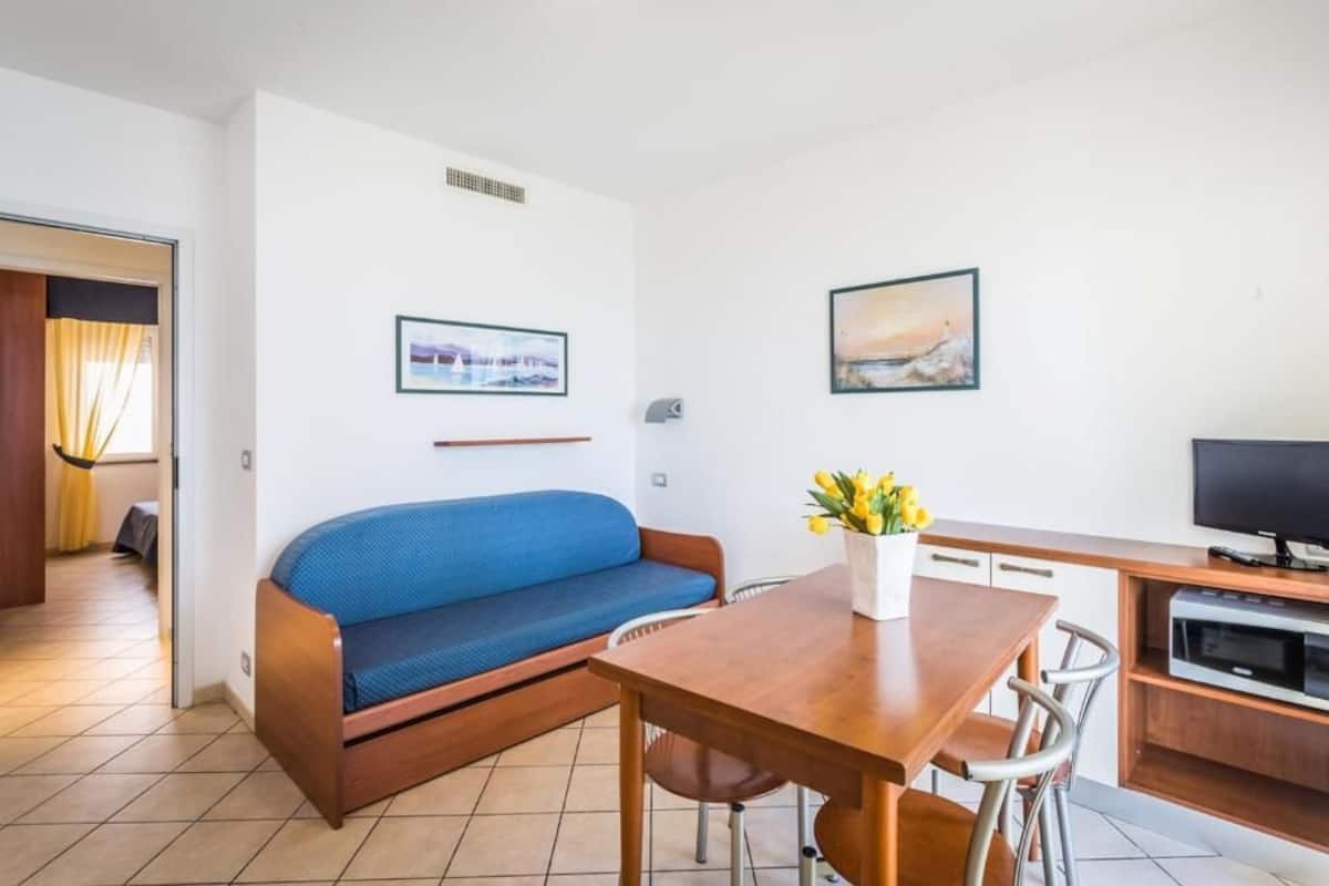 A compact living space with a sofa, a dining table, a TV, and a small kitchen area.