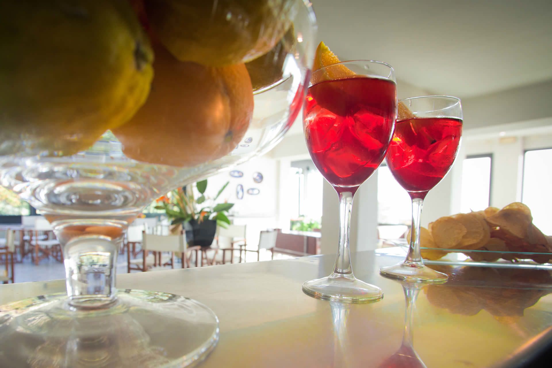 A bar area with two glasses of red beverage, a fruit bowl, and a plate with pastries.